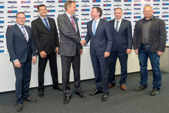 Hendrik Kampmann and Andre Gebken shake hands to symbolically mark the signing of the contract, the other four men are smiling into the camera